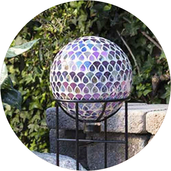 A blue and purple mosaic gazing ball on a tall black stand in a garden area.